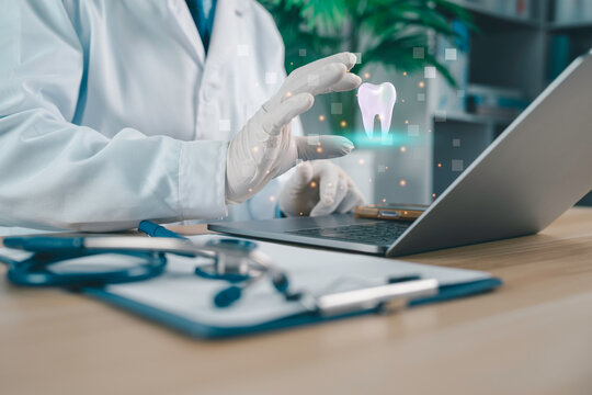 Dentist using laptop with digital tooth hologram, modern dental technology, oral healthcare innovation