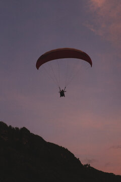 Tandem paraglider flying over hill at dusk, Uluwatu, Bali, Indonesia