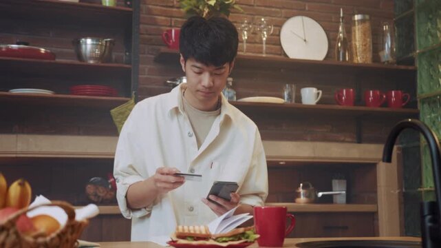 Asian man uses mobile banking, Person in kitchen focusing on phone to verify bills using banking application