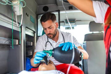 Male paramedic using a manual resuscitator bag to help a patient breathe inside an ambulance....