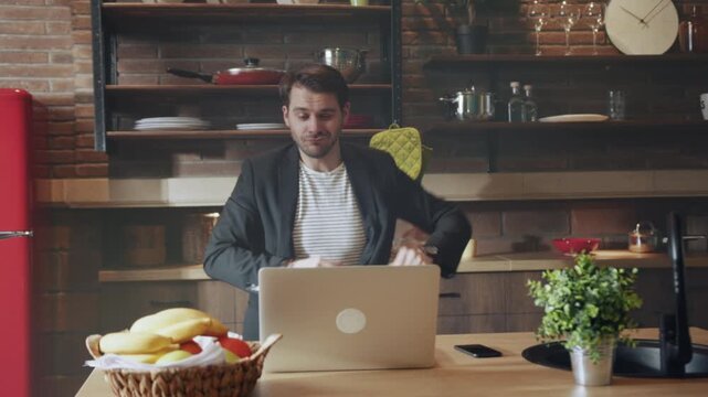 Focused male presenter rehearsing virtual meeting pitch amid kitchen setting with lively gestures and vibrant background