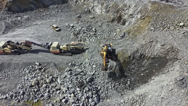 Workers use heavy machinery to extract granite at a quarry. Several trucks and equipment are present as large rocks are moved and processed for mining purposes.