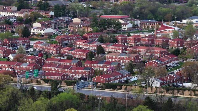 Dense Baltimore neighborhood with rows of red brick townhouses, nearby roadway traffic and urban residential patterns in typical East Coast American city setting. Aerial wide shot. Busy highway road.