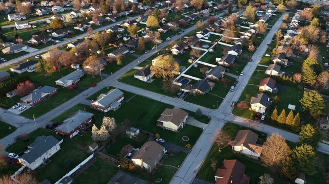 Quiet American suburban neighborhood at sunset, with classical single-family homes, driveways, tree-lined streets and warm spring colors. Peaceful residential scene. Aerial drone flyover.