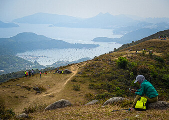 Fototapeta premium Hong Kong hikers resting on a hilltop overlooking a coastal bay with islands and boats in the distance.