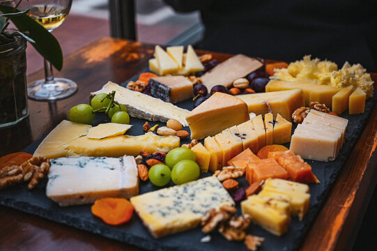 Assorted cheese board with grapes, nuts and dried fruit served on a slate platter in a restaurant setting.