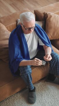 Curing respiratory disease or hypertension at home, elderly man taking pills, cozy interior. Sick aged male person unpacking medicine, modern technology of medicine for stay healthy in old age