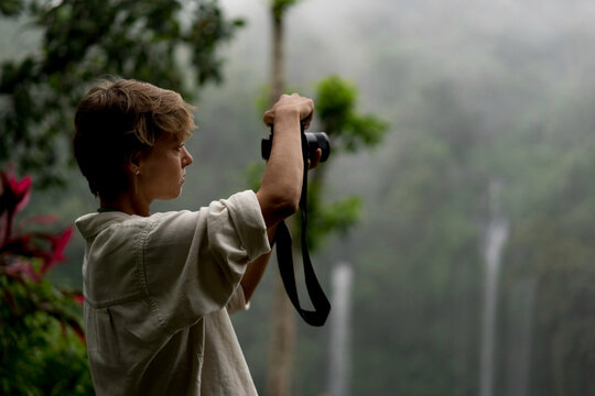 Young female photographer shooting misty jungle waterfall, Bali