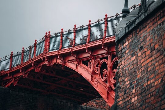 A detailed view showcases the ornate red ironwork of a historic bridge against a cloudy sky.