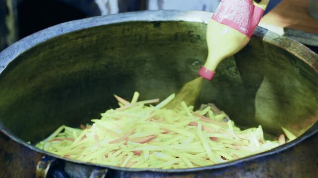 Chef in gloves seasoning pilaf in huge old metal cauldron, close-up