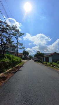 First-person video of a motorcycle ride on a sunny day on a countryside road that rises upwards and is surrounded by trees and plantations. Footage riding on the hinterland of Bandung, Indonesia