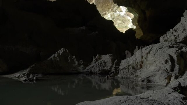 Tilt up reveal from pools of water, with light coming from left of screen from one cave opening, tilting up to reveal second cave opening in the distance with light shining in.