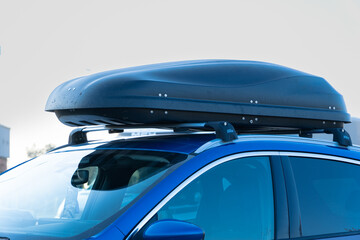 Close-up of a black aerodynamic roof cargo box mounted on a blue car's roof rack. A practical solution for extra luggage space, perfect for travel, skiing trips, and family road adventures. © Kamil