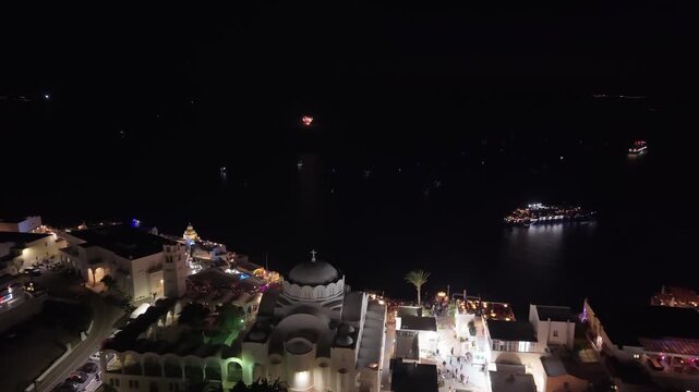 A night view of the Ifestia Festival, revealing the bustling center of Fira while spectacular fireworks erupt from the volcano, reenacting Santorini's historic volcanic eruption.