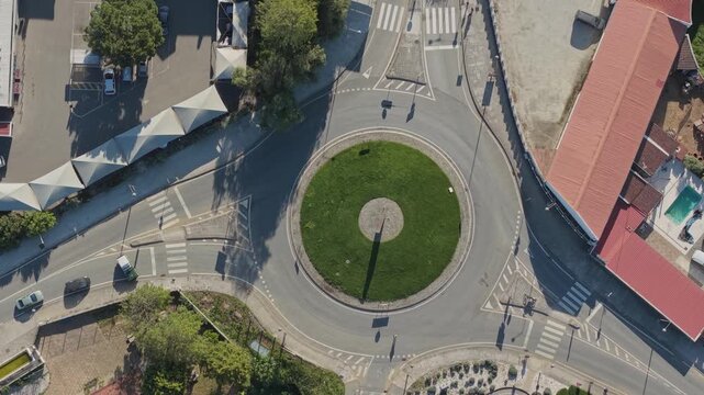 Top down drone view of cycling race riders crossing roundabout with urban streets and traffic layout