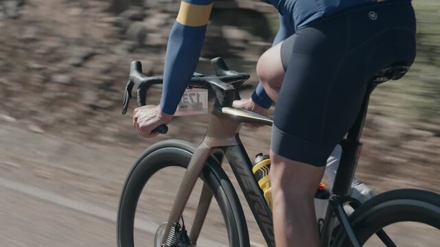 Dynamic tracking shot of cyclist riding at speed during road cycling race, close detail