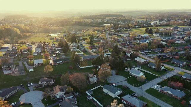 Peaceful Pennsylvania suburb at sunrise, with cul-de-sac streets, family homes, green gardens and soft morning fog. Warm and idyllic spring atmosphere in suburbia. Aerial backwards wide shot.