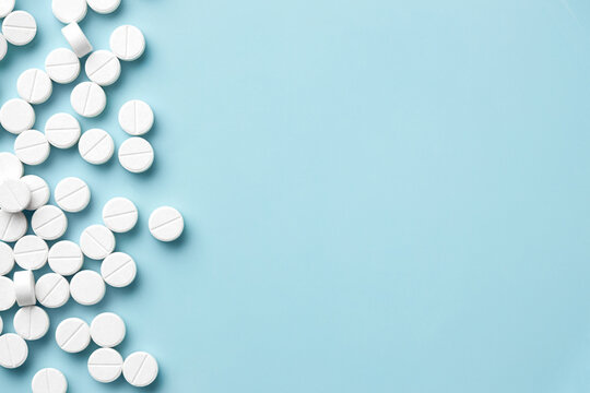 White pills scattered on light blue background, pharmacy and healthcare medication concept with ample copy space in minimalist flat lay.