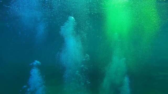 Vibrant green and blue underwater scene with rising bubbles illuminated by sunlight