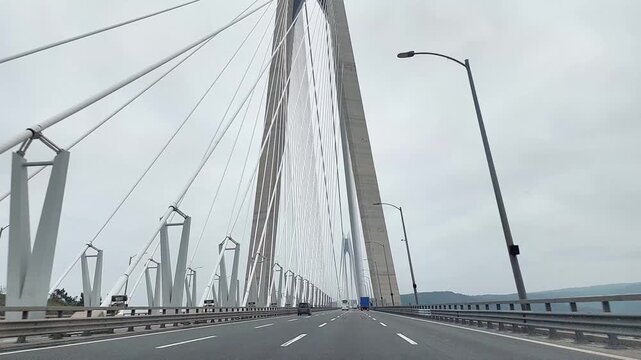 Cable stayed bridge with tall pylons and diagonal suspension cables spans roadway over water under cloudy sky, showcasing modern engineering, transport, and urban infrastructure