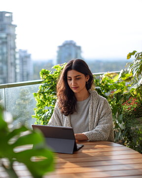 Focused young South Asian woman, a digital artist, working on her tablet outdoors on a sunny day.