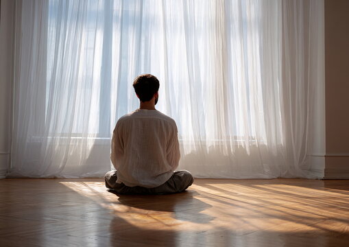 Man of Middle-Eastern descent meditating in sunlit room by a window with white curtains