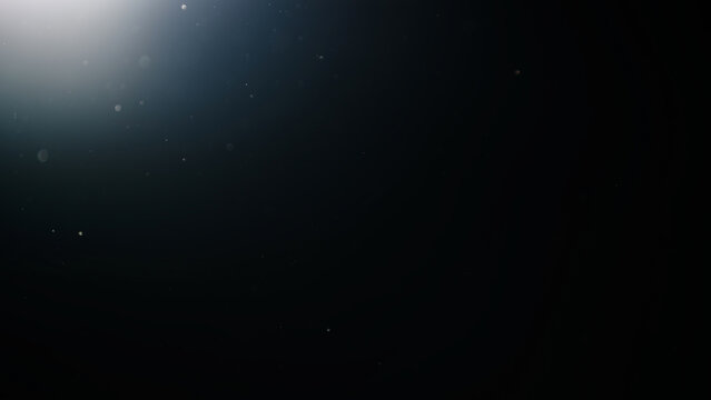 dust particles floating mid air over dark background with some lens flare