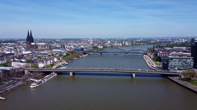 Wide drone panorama of Cologne skyline with Rhine River, multiple bridges and Cologne Cathedral. Urban European cityscape with waterfront, transport links and historic architecture.