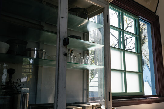 昭和レトロな医院の窓辺に置かれたアンティークな薬品棚と並べられた古いガラス瓶