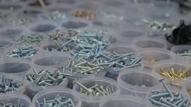 Close up shot of various metal screws and bolts of different colors organized in small plastic jars at a hardware stall in India. Ideal for construction, DIY, and industrial supply concepts.