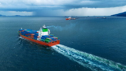 large cargo container ship leaving a white wake as it sails towards a dramatic dark storm and heavy rain over the ocean. Concept of navigating supply chain challenges, maritime resilience