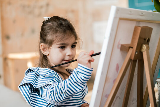 little girl holds a paint brush in her hand and drows
