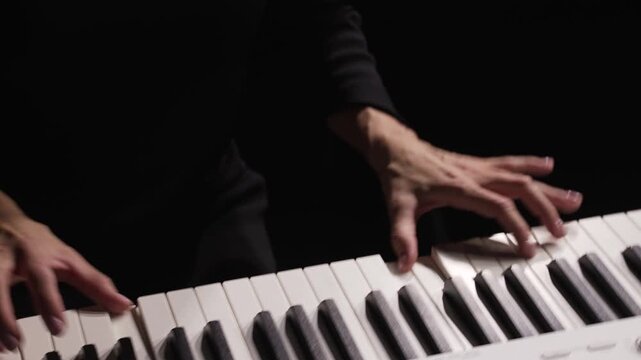 Woman plays the keys in the dark. Close-up of the pianist's hands.