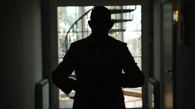 Silhouette of groom in classic suit and jacket in dark hotel hallway. The man walks down the hallway.