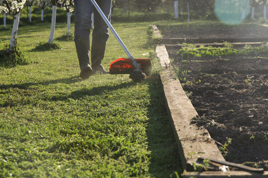 Man Trimming Grass With String Trimmer in Countryside Yard &ndash; Spring Work and Lifestyle Concept