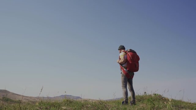 A man walks across a field with a parachute pack on his shoulders. A lover of extreme sports on a solo hike in the countryside.