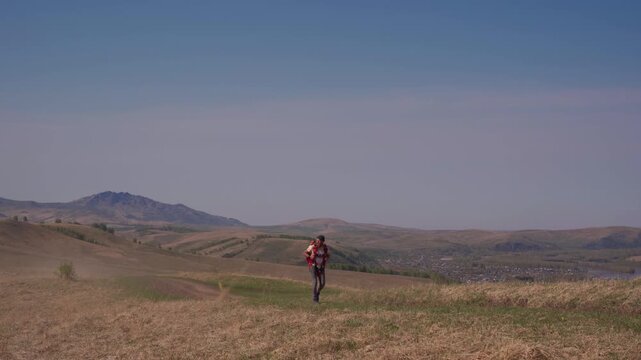 A man walks across a field with a parachute pack on his shoulders. A lover of extreme sports on a solo hike in the countryside.