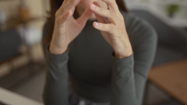 Woman interlaces fingers, hands folded on a cafe table while leaning forward in a contemplative closeup pose; quiet thoughtful.