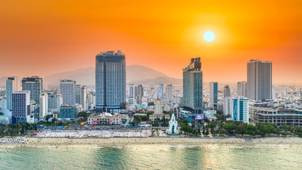 Fototapeta premium Beachfront scene in Nha Trang, Vietnam at sunset, where crowds of locals and tourists relax along the sandy shore. Rows of blue sun loungers line the beach, while people swim, stroll