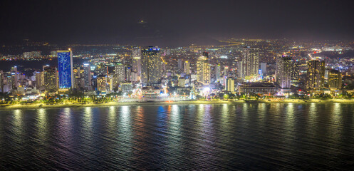 Fototapeta premium Night view of Nha Trang, Vietnam showcasing a bustling beachfront illuminated by city lights. The skyline of modern high-rise buildings glows against the dark sky, while the lively promenade