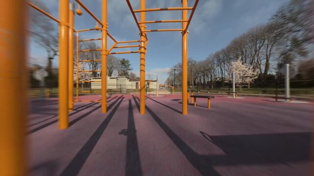 A low altitude FPV drone flight through golden, yellow playground monkey bars and jungle gym under bright sunshine, capturing fast, playful motion in a park. The camera dolly in through the poles.