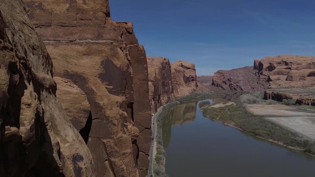 Upper Colorado River along UT128 near Moab Utah USA with close view of Wingate Sandstone cliffs and river corridor in Colorado Plateau desert, drone descent reveal shot, sandstone extreme close up