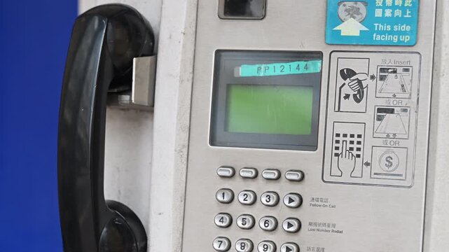 Close-up of a functional public payphone on a Hong Kong street. Shot illustrates the persistence of analog communication and essential emergency infrastructure in the smartphone era.