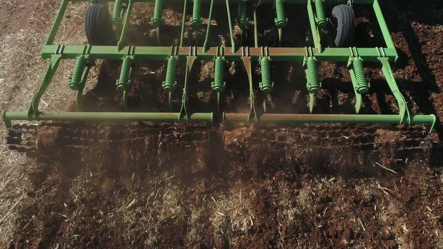 High angle closeup follows field cultivator tilling farmland soil