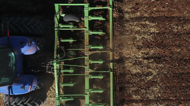 Aerial looks down onto cultivator working soil in agriculture field