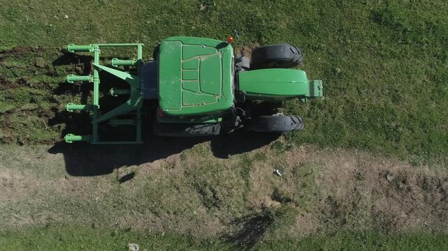 Green tractor pulls ripper tiller to loosen compacted topsoil, aerial