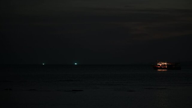 Single lit boat drifts in darkness off Tubkaek Beach