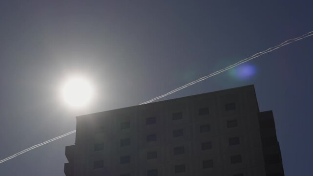 Sun Flare Behind a contemporary High-Rise Residential Complex in London, UK. Ideal for real estate marketing, urban lifestyle, or city living content. Plane Contrail in Background.