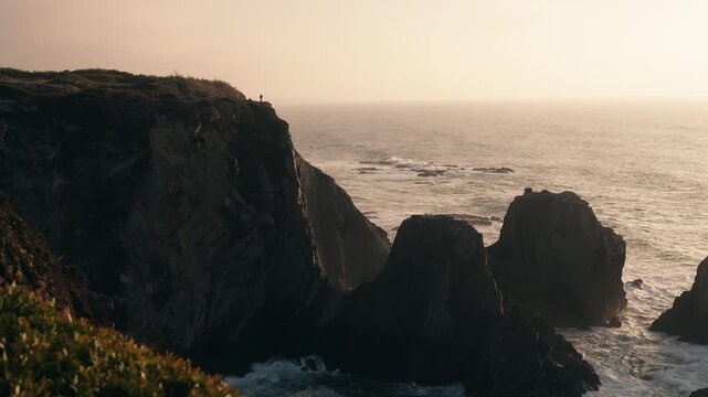 Silhouette of a fisherman standing on a cliff overlooking the ocean in Algarve Portugal.