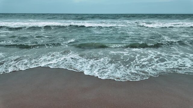 Cloudy day at beach, watching ebb and flow of waves. Slowmo